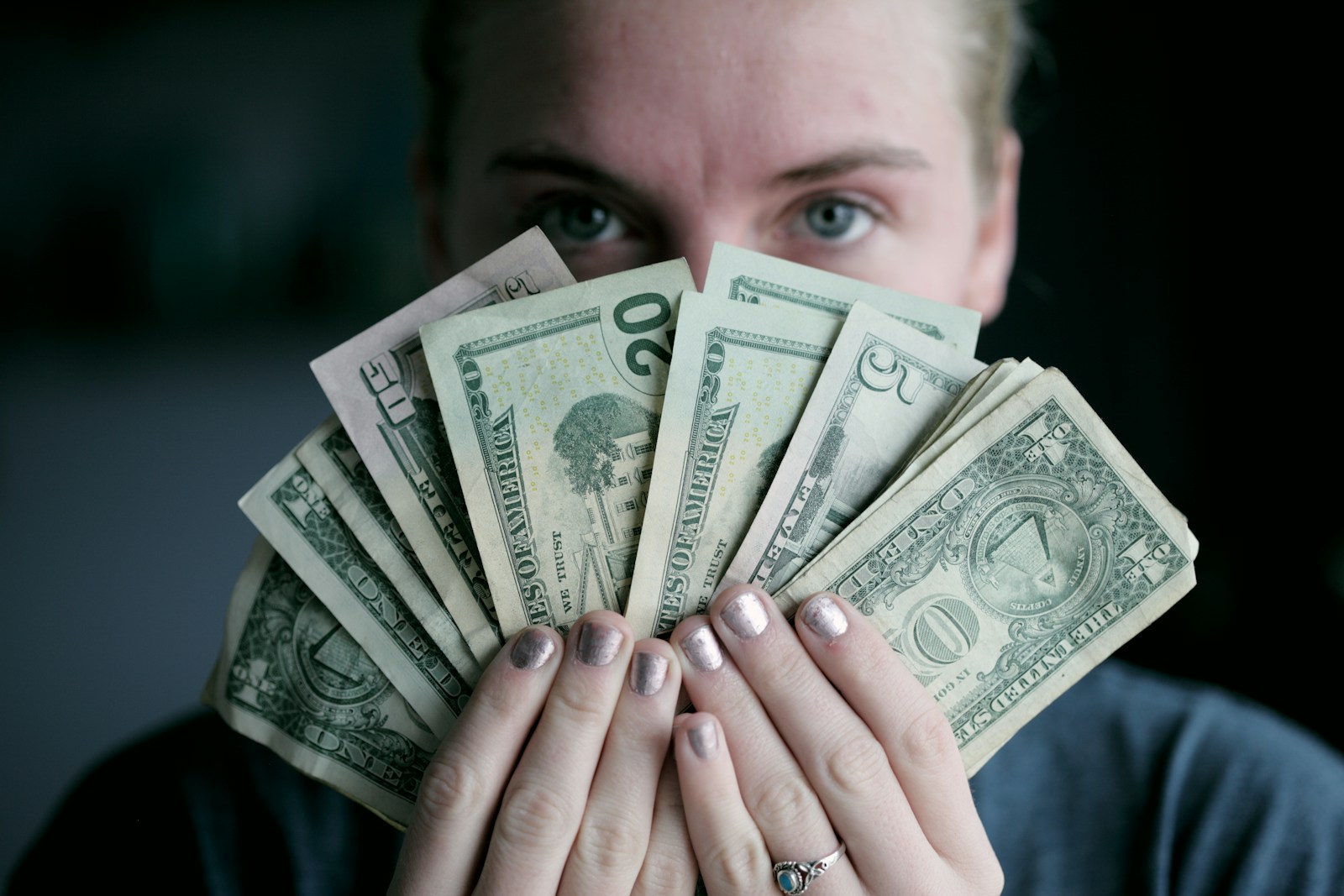 person holding fan of U.S. dollars banknote explaining why Might Proper Insurance Coverage Cost More in Today’s Economy?